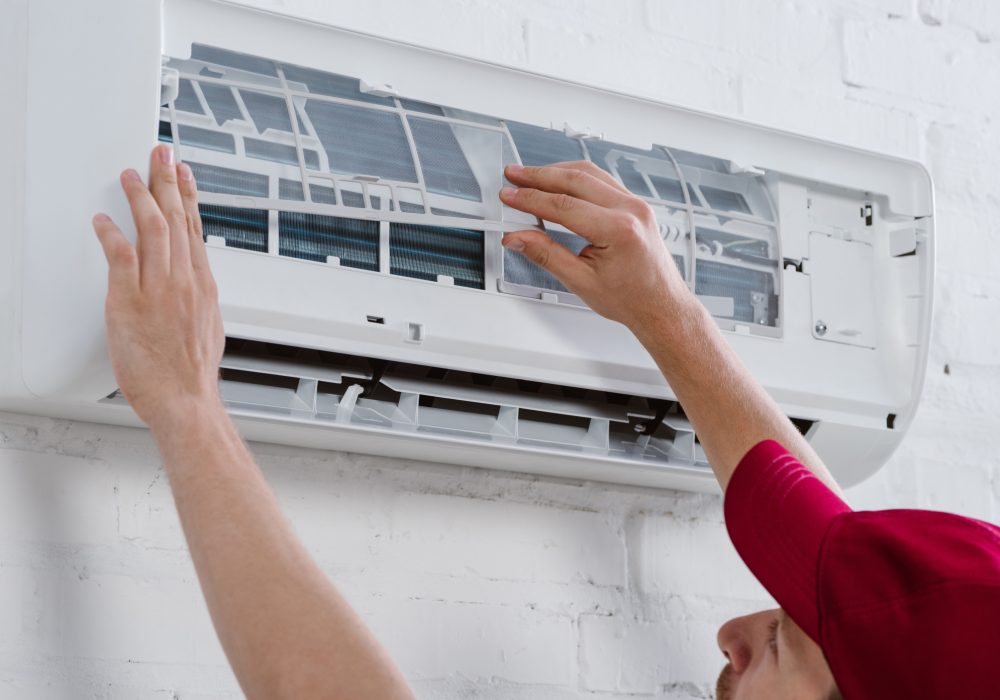close-up shot of professional repairman changing filter for air conditioner hanging on white brick